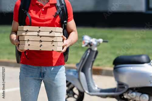 Cropped view of deliveryman with thermo backpack holding pizza boxes near blurred scooter outdoors