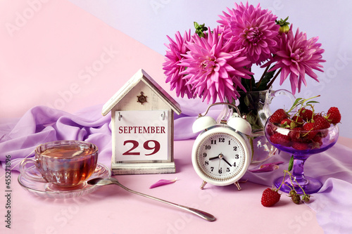 Calendar for September 29 : the name of the month in English, cubes with the number 29, a bouquet of pastel dahlias, raspberries in a cup, an alarm clock, a cup of fragrant tea photo