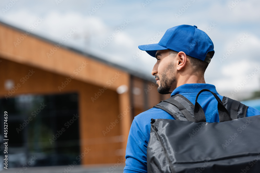 Side view of muslim deliveryman in uniform with thermo backpack outdoors Side view of muslim deliveryman in uniform with thermo backpack outdoors