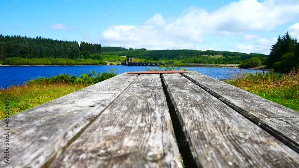 Low angle wooden plank picnic table overlooking blue sky scenic reservoir lake landscape dolly right Low angle wooden plank picnic table overlooking blue sky scenic reservoir lake landscape dolly right