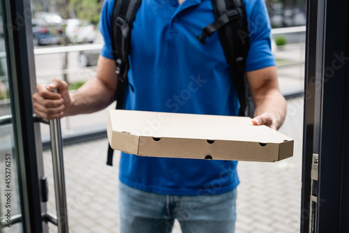 Cropped view of pizza box in hand of blurred courier near door