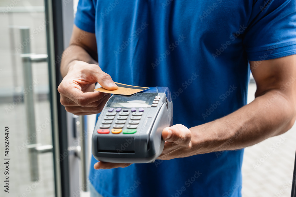 Cropped view of courier holding credit card and payment terminal outdoors Cropped view of courier holding credit card and payment terminal outdoors