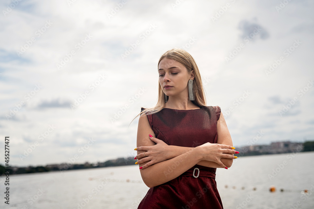 Beautiful girl in long fashionable dark red dress near pond in sity park