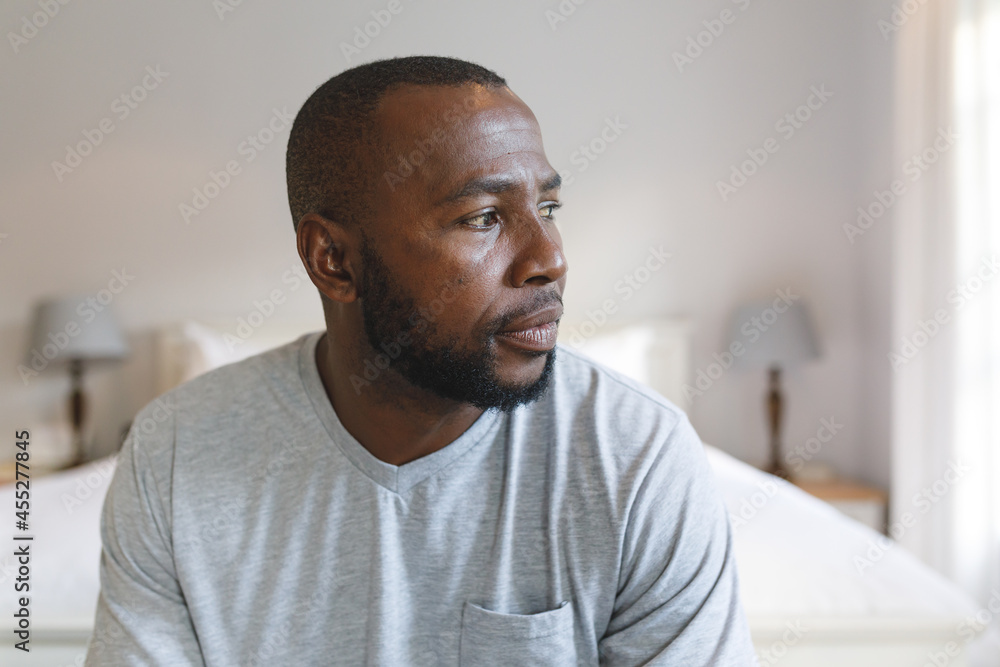 Thoughtful african american man sitting on bed and looking away in bedroom Thoughtful african american man sitting on bed and looking away in bedroom