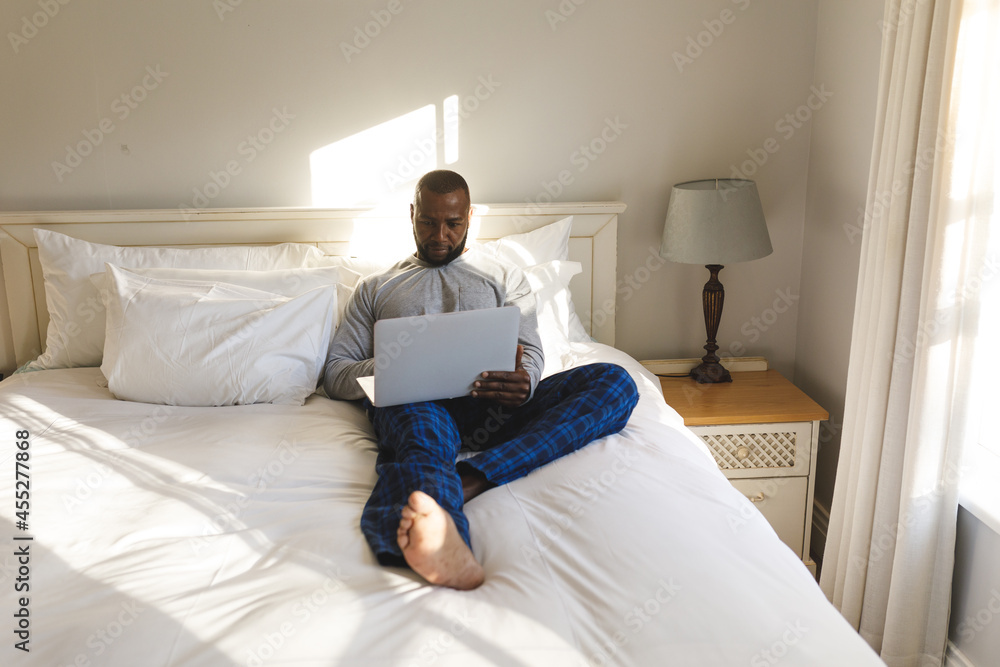 African american man using laptop and lying on bed in his bedroom African american man using laptop and lying on bed in his bedroom