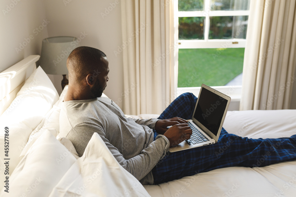 African american man using laptop and lying on bed in his bedroom African american man using laptop and lying on bed in his bedroom