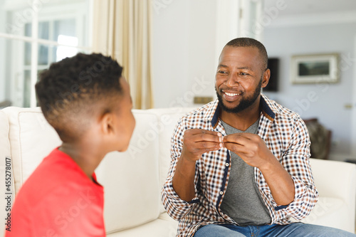 Happy african american father with son sitting on couch in living room talking sign language photo
