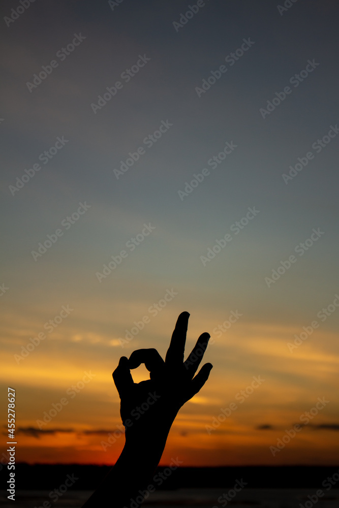 Silhouette of a man's hand during sunset making the OK symbol.