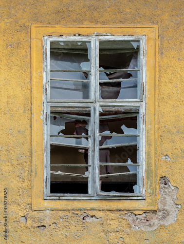 A broken old glass window with wooden frame on a facade of a ruined building.
