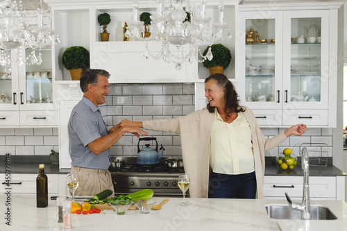 Happy senior caucasian couple in modern kitchen, dancing together and smiling