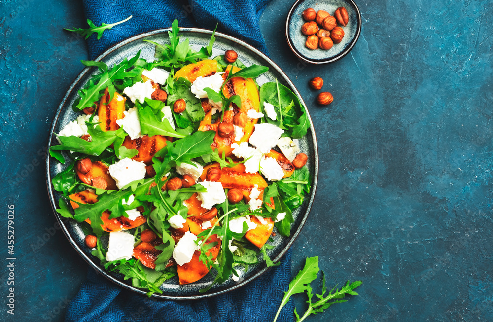 Grilled peach salad with feta cheese, hazelnuts and arugula on blue background, top view, copy space Grilled peach salad with feta cheese, hazelnuts and arugula on blue background, top view, copy space