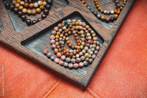 Fototapeta Naklejka Na Ścianę i Meble -  a lot of different beads made of natural semi-precious stones in the cell of a decorative wooden tray on an orange velvet background