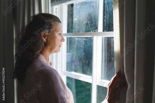 Thoughtful senior caucasian woman in bedroom, standing next to window, widening curtains Free Download Thoughtful senior caucasian woman in bedroom, standing next to window, widening curtains - GFXLoad