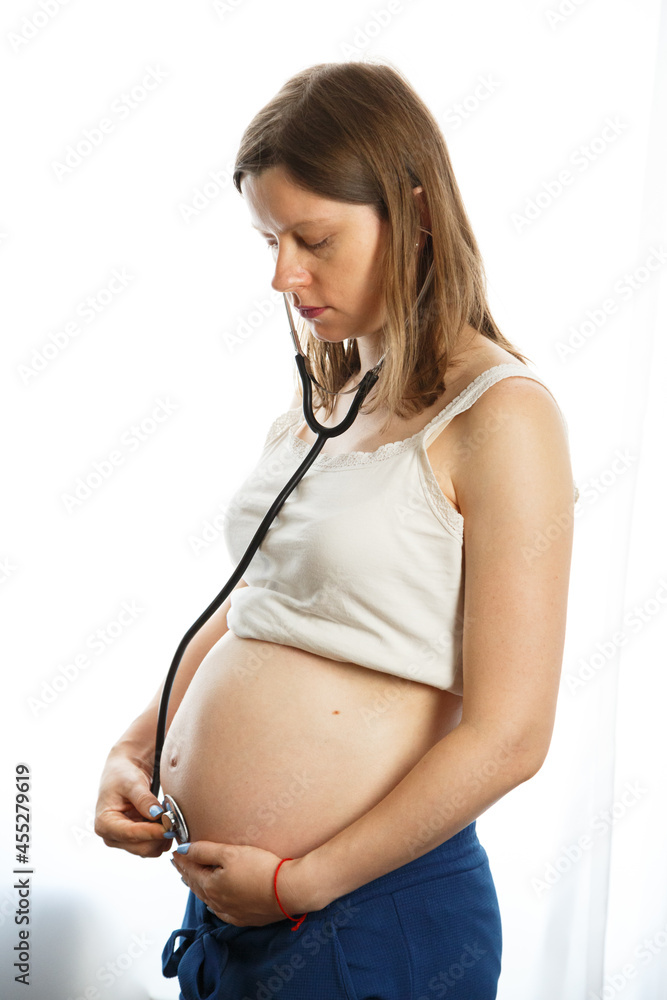 Pregnant woman with stethoscope trying to hear her baby heartbeat at home. Woman with tammy preparing for the birth of the baby. Pregnant woman with stethoscope trying to hear her baby heartbeat at home. Woman with tammy preparing for the birth of the baby.
