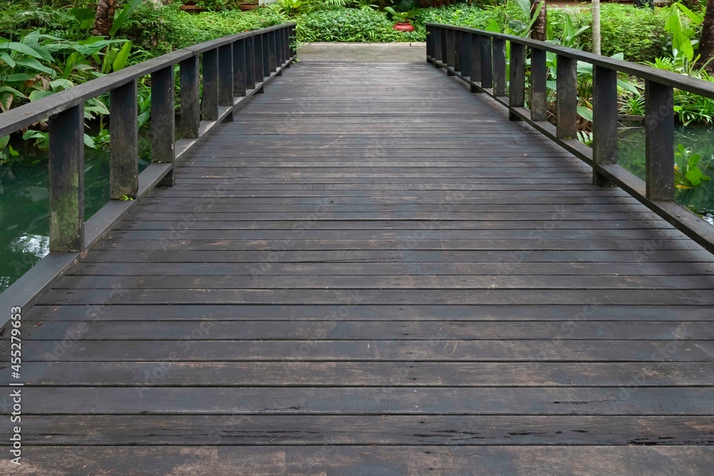 A dark wooden bridge crosses a pond in a tropical garden A dark wooden bridge crosses a pond in a tropical garden