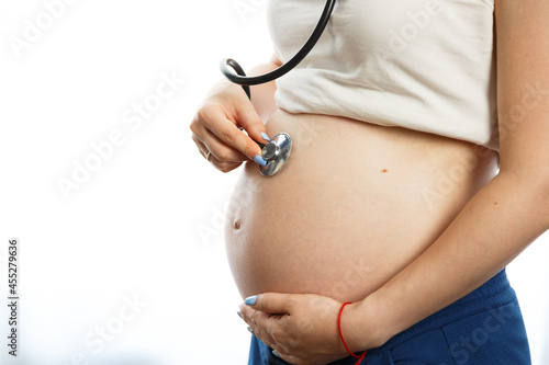 Pregnant woman with stethoscope trying to hear her baby heartbeat at home. Woman with tammy preparing for the birth of the baby. photo