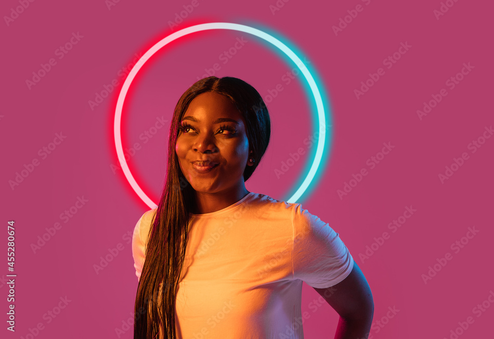 Portrait of african happy young girl in neon light on dark studio ...