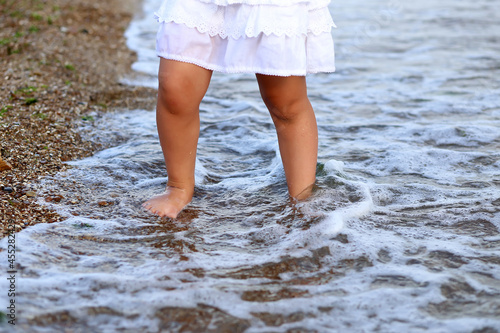 Tanned legs, barefoot feet. Happy child walks along the wet shore in sunny weather.