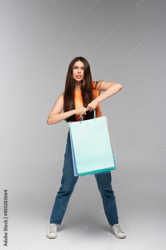 full length of stressed young woman holding shopping bags on grey full length of stressed young woman holding shopping bags on grey