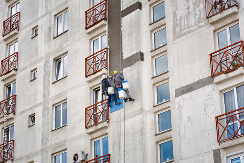 Rope access job, construction workers repair and restore facade of high building. Industrial alpinist at height on rope, plastering wall with trowel. Industrial climber repairing house facade