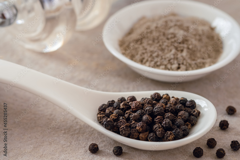 Black pepper corn on spoon and black pepper powder in bowl Black pepper corn on spoon and black pepper powder in bowl