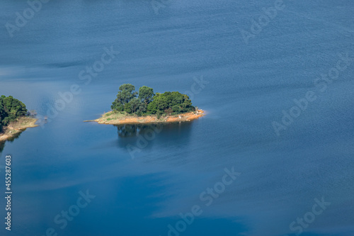 The water of the lake is blue, the trees by the lake are green, and there is an island in the lake