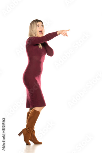 Fototapeta Naklejka Na Ścianę i Meble -  Young excited blonde in a tight red dress and leather boots pointing