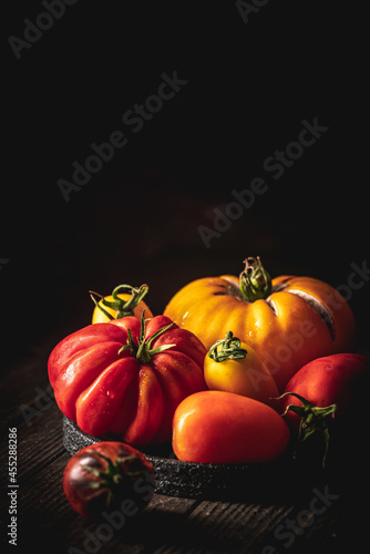 Fresh organic garden tomatoes on rustic table over dark wooden background. Healthy and vegetarian food concept.