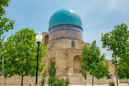 Building of Kok Gumbaz mosque as seen from side of park behind trees. Blue dome seems to be trying to merge with color of sky. Shot in Shakhrisabz, Uzbekistan photo