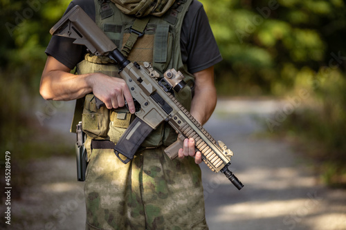 Close up of a man standing with an airsoft assault rifle in military uniform