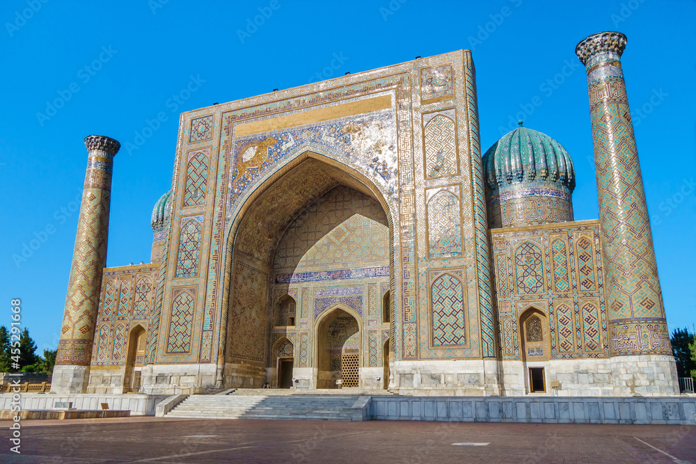 Facade of Sher-Dor Madrasah in Samarkand, Uzbekistan. Sun is reflected in ancient majolica patterns. Inscriptions on  building are quotes of suras from Koran in Arabic