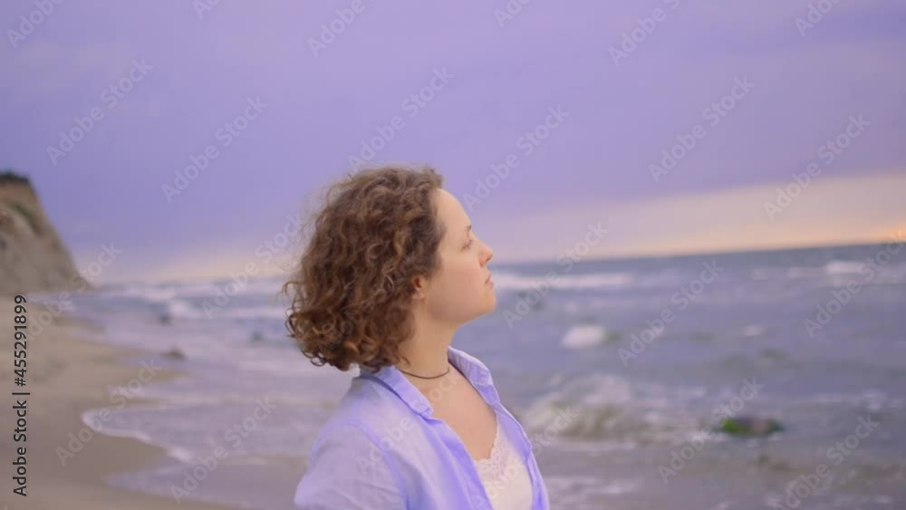 Close up lifestyle image of woman with cirly hair on sunset is standing on the beach against the backdrop of the ocean. Close up lifestyle image of woman with cirly hair on sunset is standing on the beach against the backdrop of the ocean.