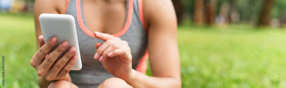 cropped view of sportswoman using smartphone in park, banner
