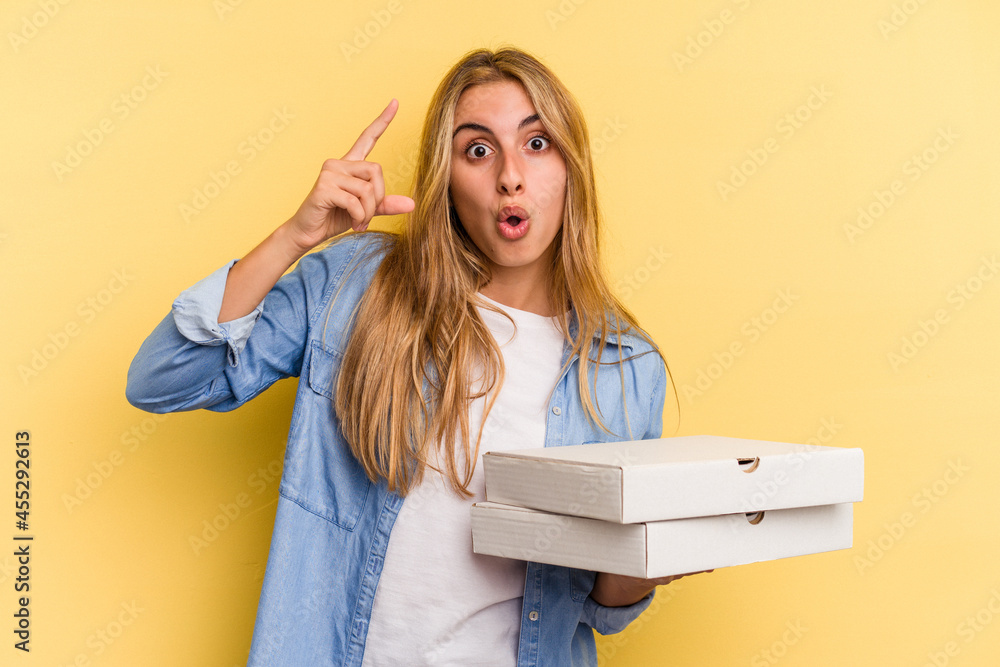 Young caucasian blonde woman holding pizzas isolated on yellow background having an idea, inspiration concept. Young caucasian blonde woman holding pizzas isolated on yellow background having an idea, inspiration concept.