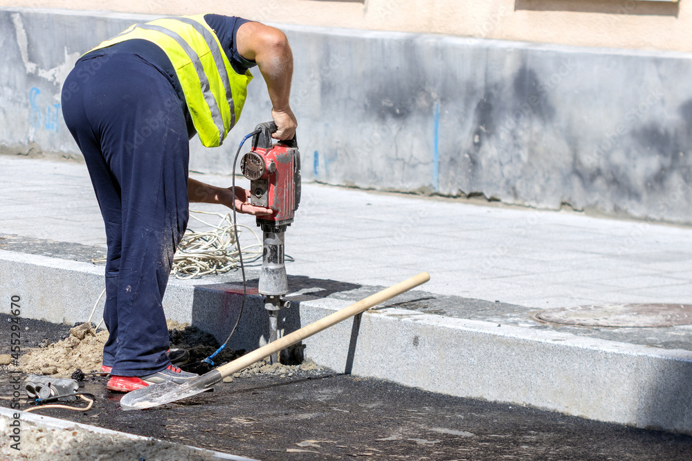 A worker makes a hole in the asphalt with a perforator in order to install a road sign. Road works. A worker makes a hole in the asphalt with a perforator in order to install a road sign. Road works.