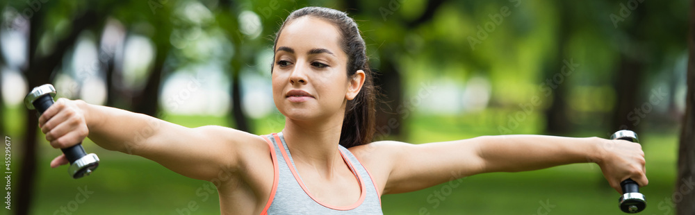 young sportswoman holding dumbbells in outstretched hands, banner young sportswoman holding dumbbells in outstretched hands, banner
