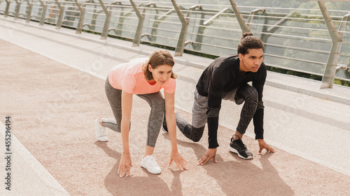 Young mixed-race couple friends athletes running jogging together in fitness outfit on city urban bridge. Burning calories workout exercises outdoors.