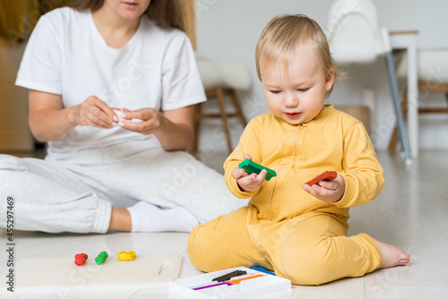 Child hands playing with colorful playdough. Moulding from plasticine on floor. Playing with clay at home. Faceless mother using modeling clay. Development toy for child motor skill