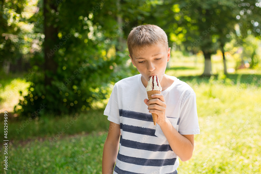 Teenager boy eating ice-cream cone on green nature background. Summer, junk food and people concept. Copyspace Teenager boy eating ice-cream cone on green nature background. Summer, junk food and people concept. Copyspace