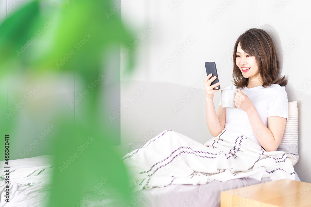 ベッドでスマホを使う若い女性 ベッドでスマホを使う若い女性