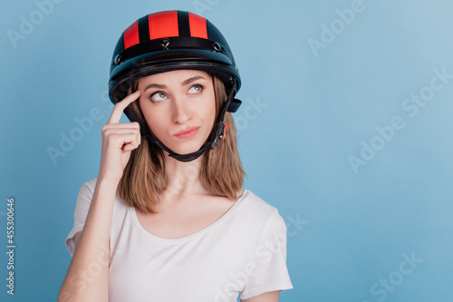 Portrait of minded doubtful biker lady wear motorcycle helmet look blank space think on blue background
