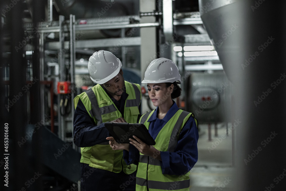 Male engineer and female engineer working together in an industrial plant room Male engineer and female engineer working together in an industrial plant room