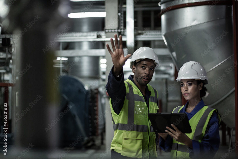 Male engineer training a female engineer in an industrial plant room Male engineer training a female engineer in an industrial plant room