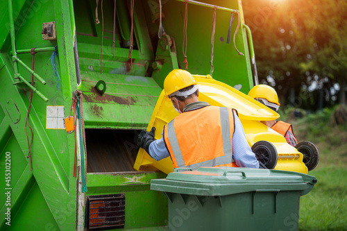 Rubbish cleaner man working with green garbage truck loading waste and trash bin at city,Waste collectors at work. photo