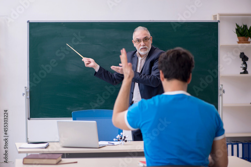 Old male teacher and young male student in front of blackboard