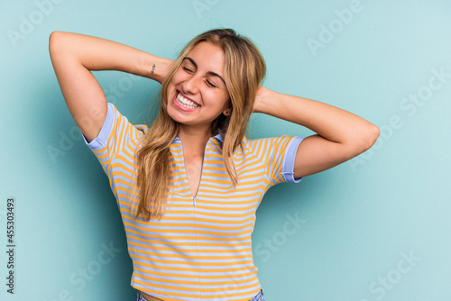 Young caucasian blonde woman isolated on blue background feeling confident, with hands behind the head.