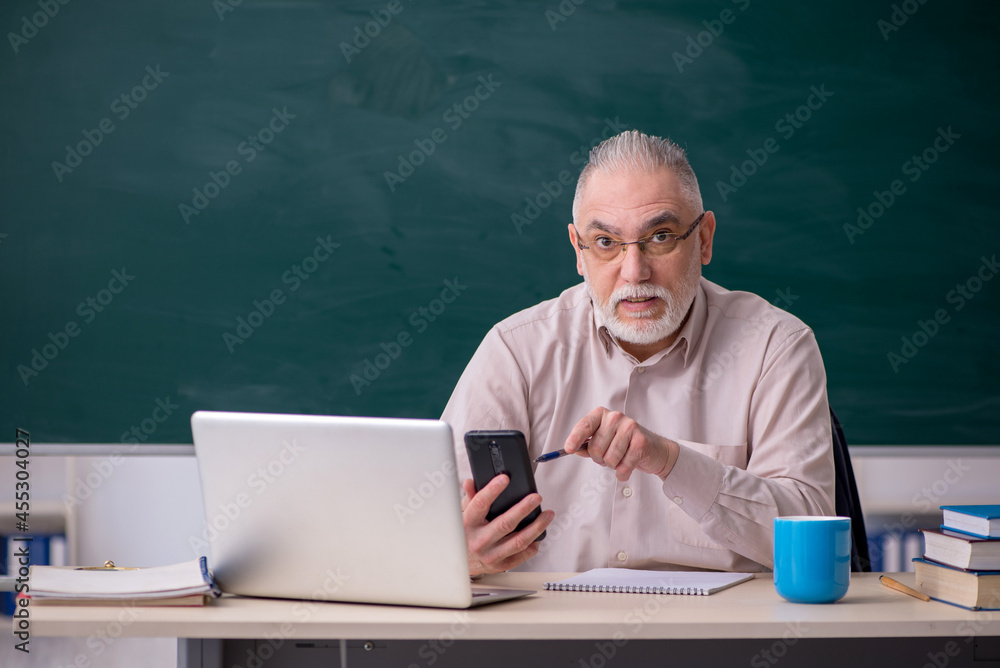 Old male teacher in front of blackboard Old male teacher in front of blackboard