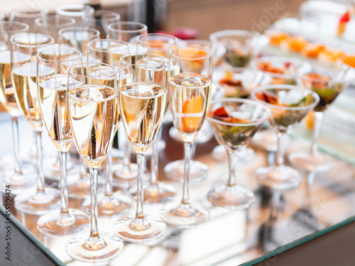 Champagne in glasses, bowls of snacks on a shiny glass table. Buffet table, served for a banquet. Catering service.