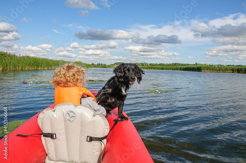 A little sporty girl in a life jacket floats on the Zdwyzh River on a red kayak with a black dog Cocker Spaniel. Ukraine