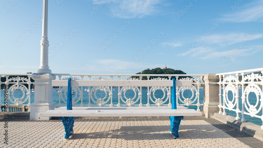 Fototapeta premium Bench on the promenade of San Sebastian, Spain. Blue sky with white clouds on the background.
